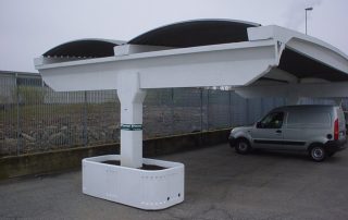 Struttura prefabbricata in cemento con copertura ondulata, utilizzata come parcheggio coperto.