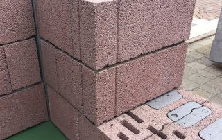 Dimostrazione di muratura con blocchi in laterizio porizzato su una piattaforma espositiva, con colonne grigie e pallet di materiali da costruzione sullo sfondo.