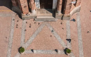 Pavimentazione in mattoni dal tono caldo con inserti in pietra chiara, disposti in un motivo geometrico davanti all'ingresso di un edificio storico.