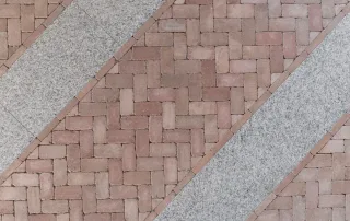 Pavimentazione con mattoni disposti a spina di pesce alternati a fasce in pietra chiara.