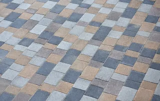 Pavimentazione in blocchi rettangolari multicolore disposti in pattern alternati con tonalità di grigio, marrone e antracite.