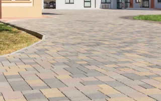 Pavimentazione in blocchi quadrati con tonalità miste di grigio, beige e marrone, disposti in un pattern regolare.