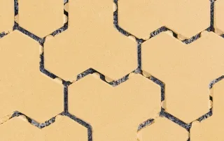 Pavimentazione drenante in cemento con blocchi ad incastro color sabbia e fughe riempite di ghiaia.
