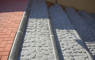 Rampa in cemento con pavimentazione a effetto ciottolato e canalette drenanti.