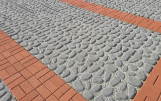 Pavimentazione in cemento effetto ciottolato con fasce in mattoncini rossi.