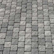 Pavimentazione in cubetti di pietra con finitura fiammata, tonalità ardesia con sfumature di grigio scuro.