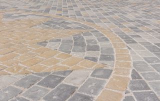 Pavimentazione in pietra con un motivo geometrico composto da lastre rettangolari e quadrate in diverse tonalità di grigio e ocra.