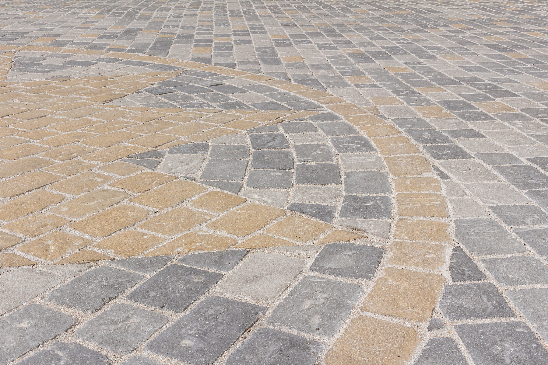 Pavimentazione in pietra con un motivo geometrico composto da lastre rettangolari e quadrate in diverse tonalità di grigio e ocra.