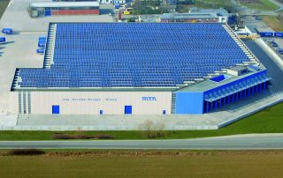 Vista aerea di un grande magazzino industriale con pannelli solari installati su tutto il tetto.
