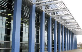 Colonne blu e struttura in acciaio di un edificio industriale con ampie superfici vetrate.