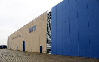 Facciata di un capannone industriale prefabbricato con pannelli di cemento e rivestimenti metallici blu.