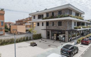 Pavimentazione in lastre di pietra chiara davanti a un edificio moderno con facciata in pietra e vetrine commerciali.