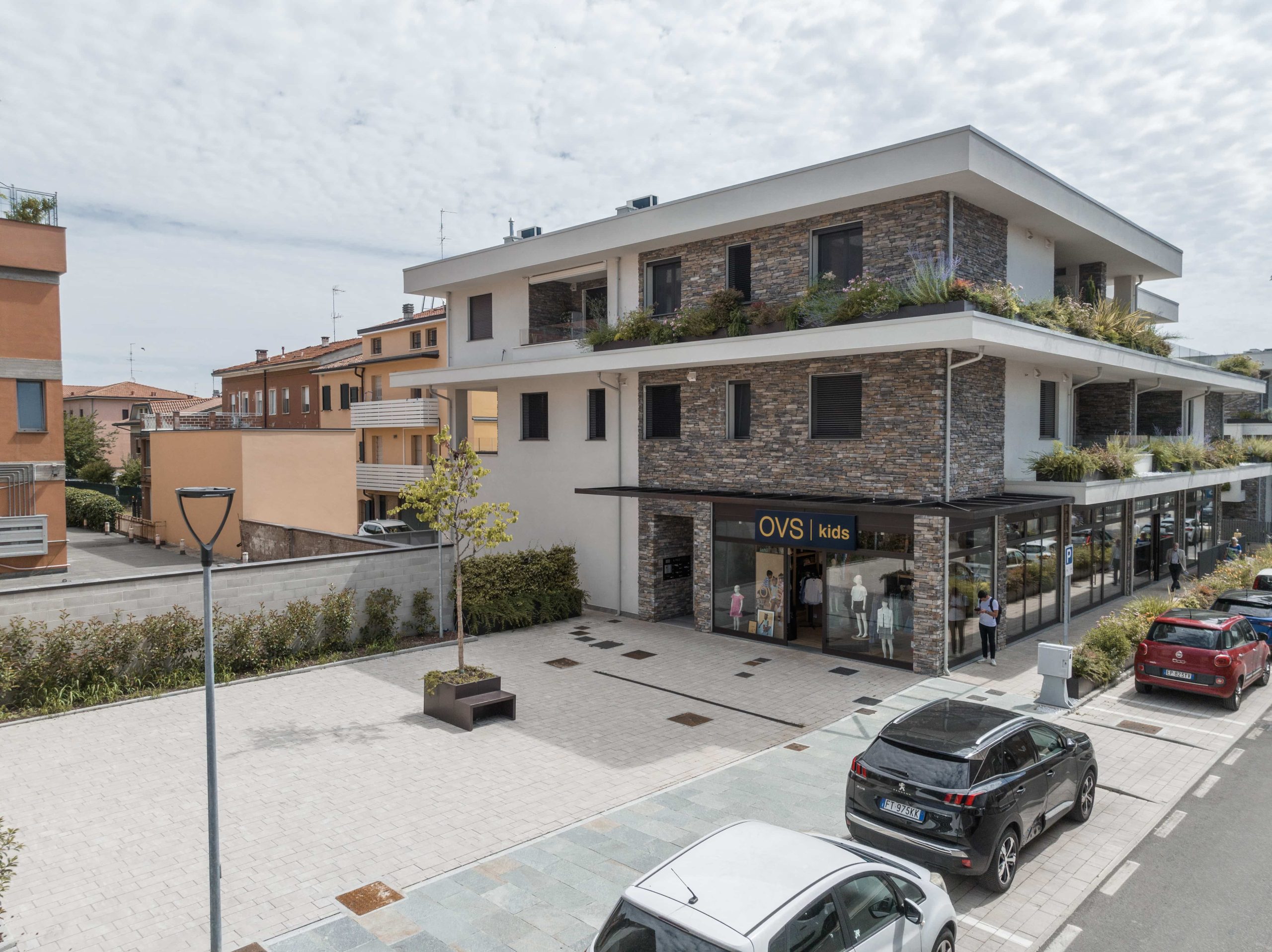 Pavimentazione in lastre di pietra chiara davanti a un edificio moderno con facciata in pietra e vetrine commerciali.
