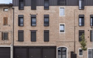 Pavimentazione in lastre di pietra naturale davanti a un edificio in mattoni ristrutturato con dettagli moderni in metallo scuro.