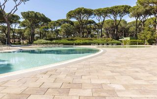 Pavimentazione in masselli autobloccanti attorno a due piscine, una più ampia e una più piccola con area giochi d'acqua.