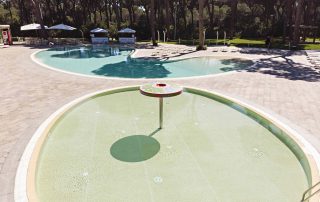 Pavimentazione in masselli autobloccanti attorno a due piscine, una più ampia e una più piccola con area giochi d'acqua.