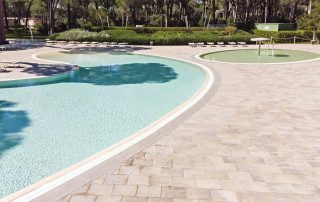 Pavimentazione in masselli autobloccanti attorno a due piscine, una più ampia e una più piccola con area giochi d'acqua.