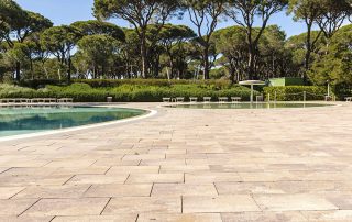 Pavimentazione in masselli autobloccanti attorno a due piscine, una più ampia e una più piccola con area giochi d'acqua.