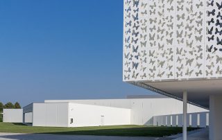 Pavimentazione in lastre rettangolari chiare con linee sottili di separazione, davanti a un edificio moderno bianco con pannelli decorati da motivi di farfalle.