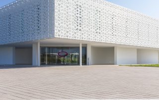 Pavimentazione in lastre rettangolari chiare con linee sottili di separazione, davanti a un edificio moderno bianco con pannelli decorati da motivi di farfalle.