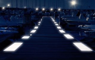 Pontile in legno illuminato da luci a LED integrate nella pavimentazione.Il molo è circondato da numerose imbarcazioni ormeggiate.