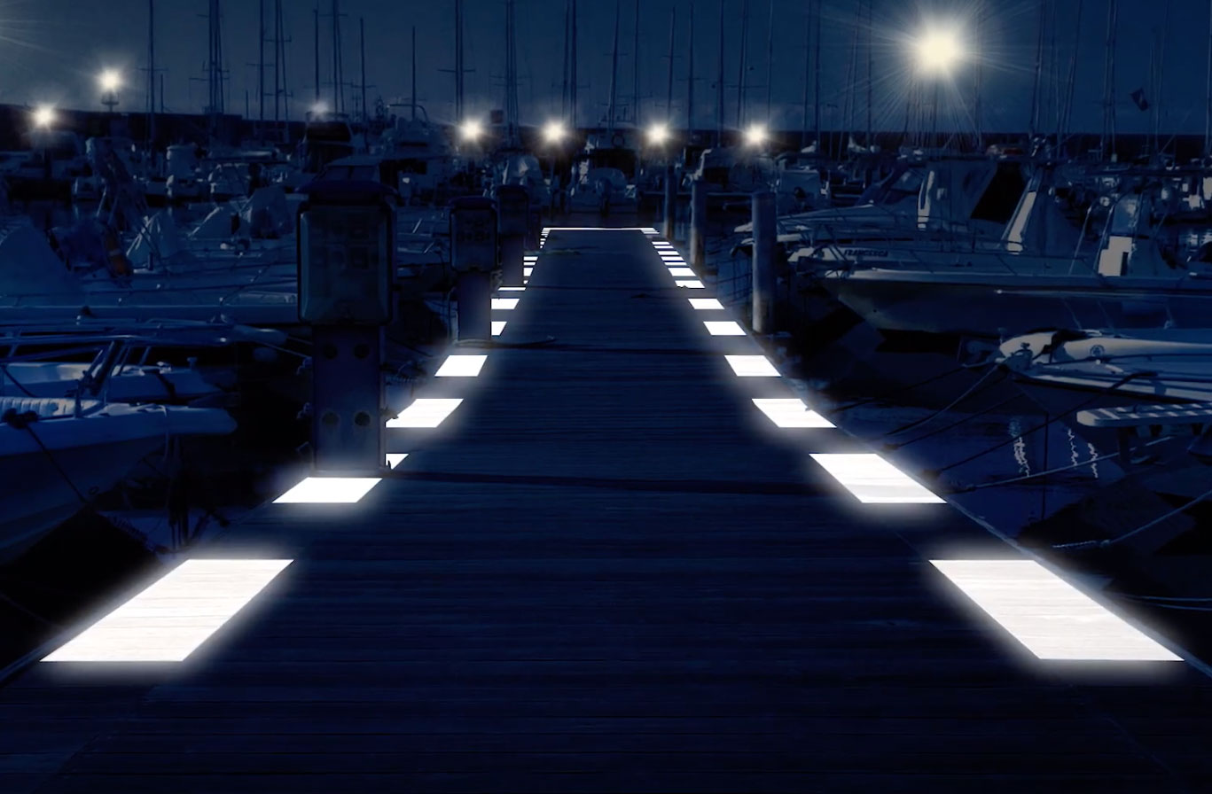 Pontile in legno illuminato da luci a LED integrate nella pavimentazione.Il molo è circondato da numerose imbarcazioni ormeggiate.