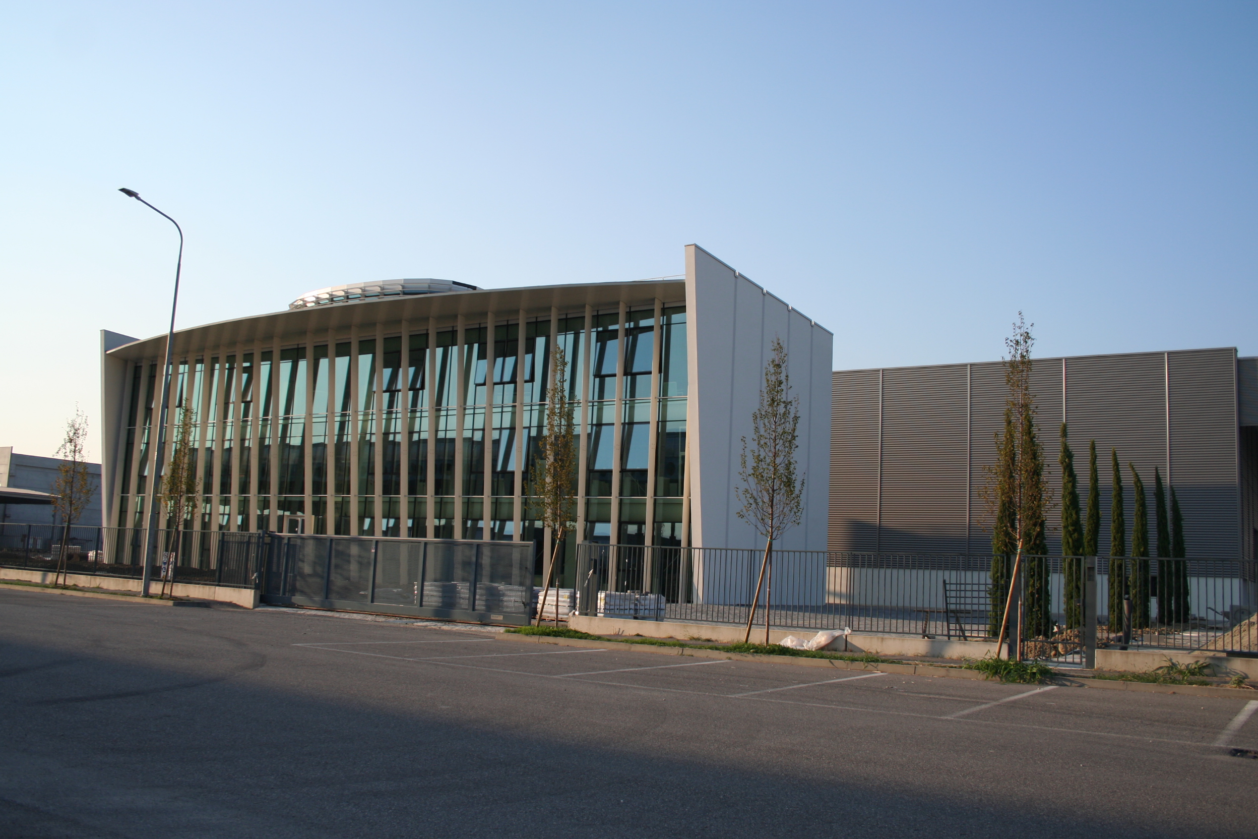 Edificio moderno con ampia facciata in vetro e struttura inclinata in metallo, affiancato da una sezione con pannelli metallici.