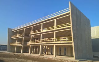 Edificio prefabbricato in cemento armato in fase di costruzione, con struttura a tre piani e parapetti di sicurezza in legno.