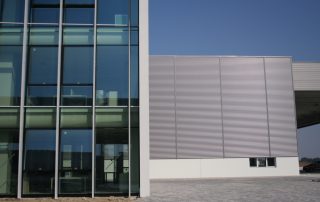 Dettaglio della facciata di un edificio moderno con ampie vetrate e una sezione laterale in pannelli metallici.