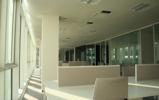 Ufficio moderno e luminoso con open space, arredato con postazioni di lavoro bianche e pareti divisorie in vetro.