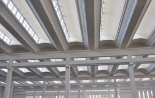 Soffitto di un capannone industriale con travi bianche.