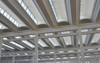 Soffitto di un capannone industriale con travi bianche.