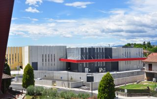 Struttura industriale con pannelli prefabbricati in cemento di diverse tonalità, finestre verticali strette e una pensilina rossa .