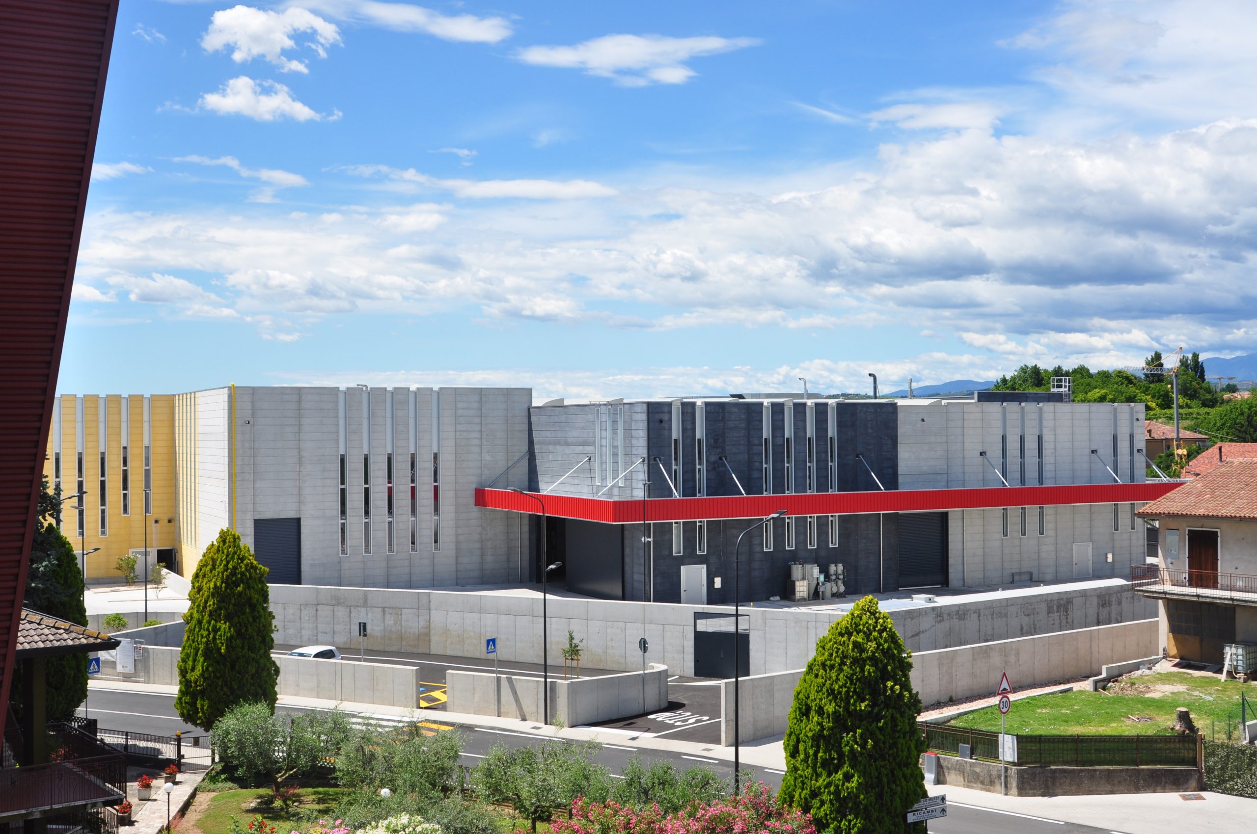 Struttura industriale con pannelli prefabbricati in cemento di diverse tonalità, finestre verticali strette e una pensilina rossa .