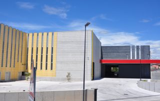 Struttura industriale con pannelli prefabbricati in cemento di diverse tonalità, finestre verticali strette e una pensilina rossa .