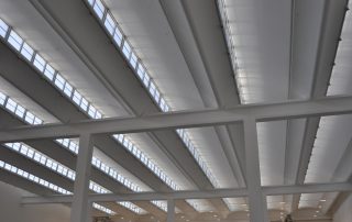 Soffitto di un capannone industriale con travi bianche.