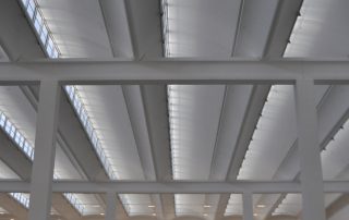 Soffitto di un capannone industriale con travi bianche.