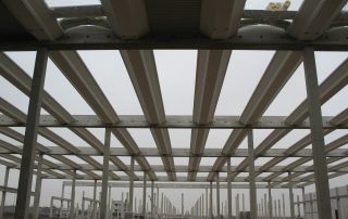 Struttura prefabbricata in costruzione con travi in cemento armato e copertura parziale.