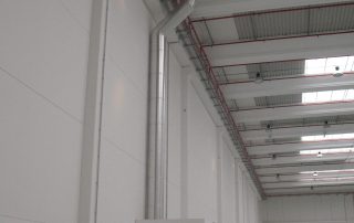 Interno di un capannone industriale con pareti bianche, impianto di ventilazione in acciaio, tubature a soffitto.