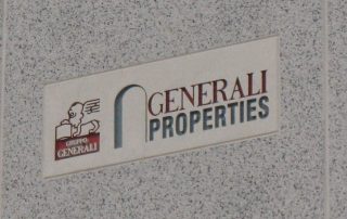 Insegna "Generali Properties" su una parete in cemento, con il logo del Gruppo Generali raffigurante un leone alato con un libro.