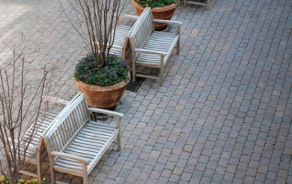 Vista dall'alto di una pavimentazione in pietra con panchine in legno e grandi vasi di terracotta contenenti piante e fiori.