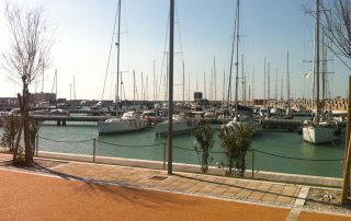Pavimentazione pedonale in pietra e materiale drenante lungo un porto turistico.