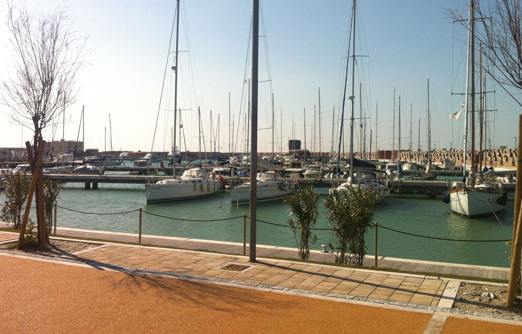 Pavimentazione pedonale in pietra e materiale drenante lungo un porto turistico.