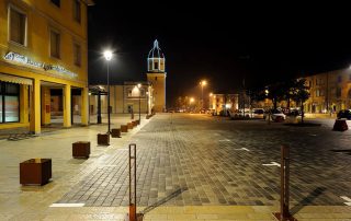 Piazza urbana illuminata di notte con pavimentazione in pietra.