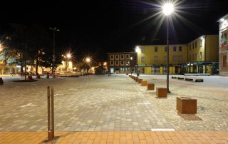 Piazza urbana illuminata di notte con pavimentazione in pietra.