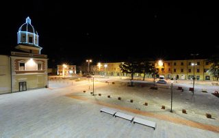 Piazza urbana illuminata di notte con pavimentazione in pietra.