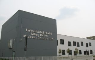 Edificio prefabbricato dell'Università degli Studi di Milano Bicocca, Medicina e Chirurgia U18, con facciata moderna in pannelli grigi e bianchi, finestre nere incassate e recinzione metallica.