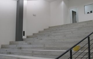 Interno di un edificio prefabbricato con gradinate in cemento grezzo.