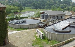 Impianto di depurazione con vasche circolari prefabbricate in cemento, edifici tecnici e aree di trattamento delle acque.