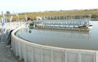 Passerella sopra una vasca industriale di trattamento delle acque, con corrimano e impianti tecnici installati.